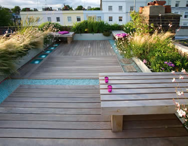 Elevated wooden deck with purple flowers, ornamental grasses, and seating area overlooking cityscape