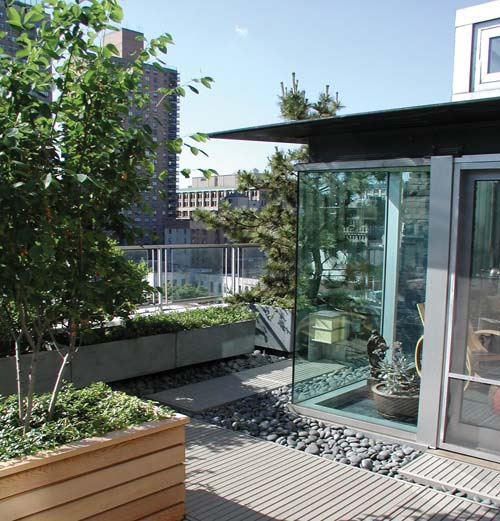 Modern rooftop deck with wooden planters, green plants, glass doors, and city views.