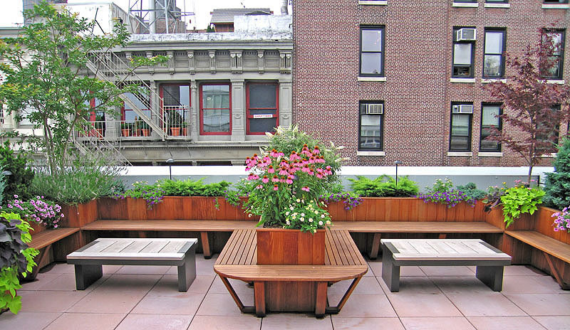 Urban rooftop garden with wooden benches, flowering planters, and brick building backdrop