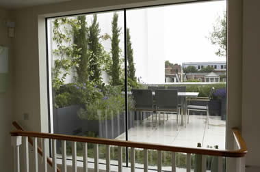 Modern glass sliding doors opening to a rooftop deck with outdoor furniture and green plants