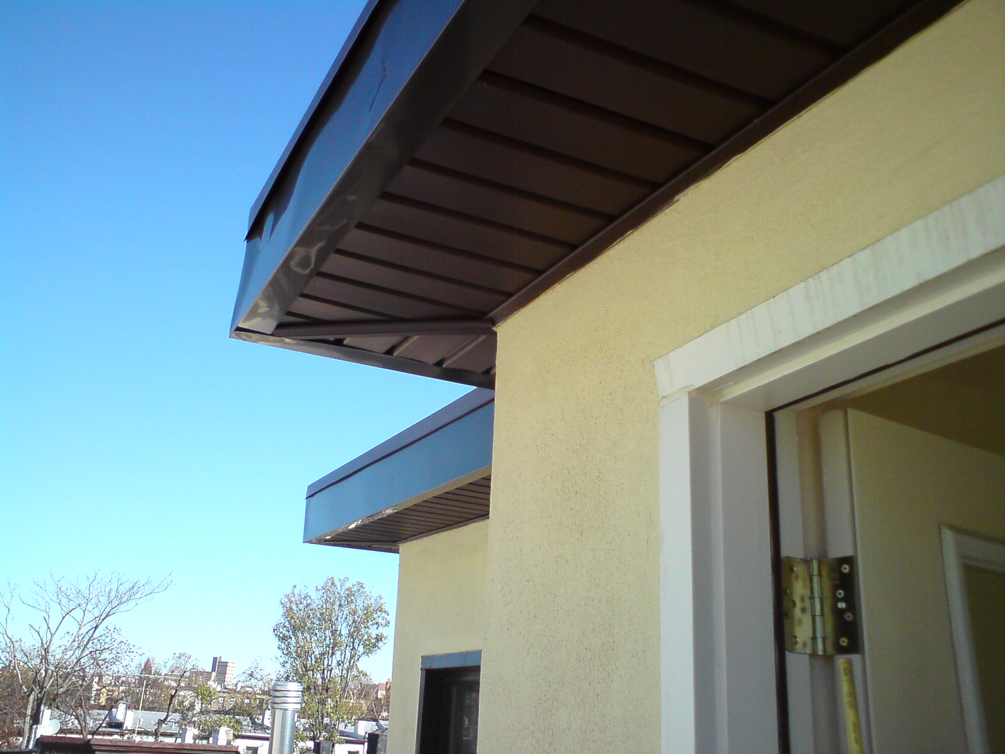 Modern rooftop deck with blue metal awning and yellow stucco building wall, city skyline background