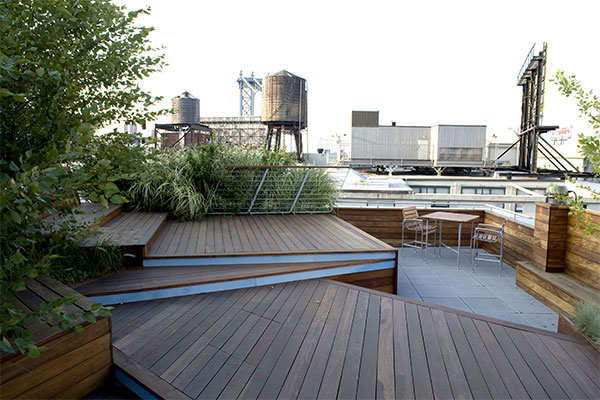 Modern rooftop deck with wooden decking, blue accents, industrial Brooklyn skyline beyond