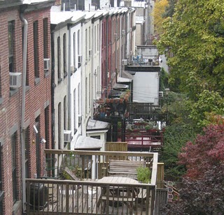 Elevated view of Brooklyn rooftop deck with wooden railings, potted plants, and surrounding historic brick buildings.