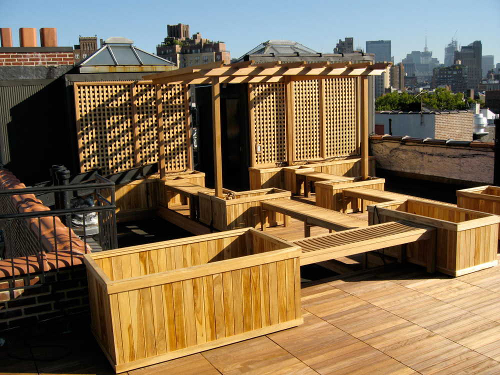 Modern wooden pergola and seating areas on sunny urban rooftop with city skyline.