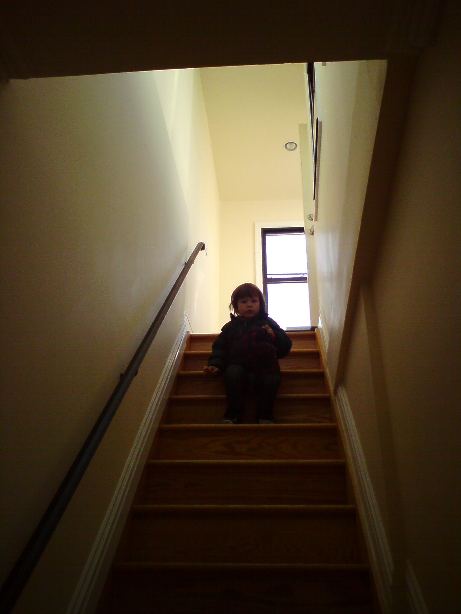 Young child sitting on wooden staircase with natural light from window above.