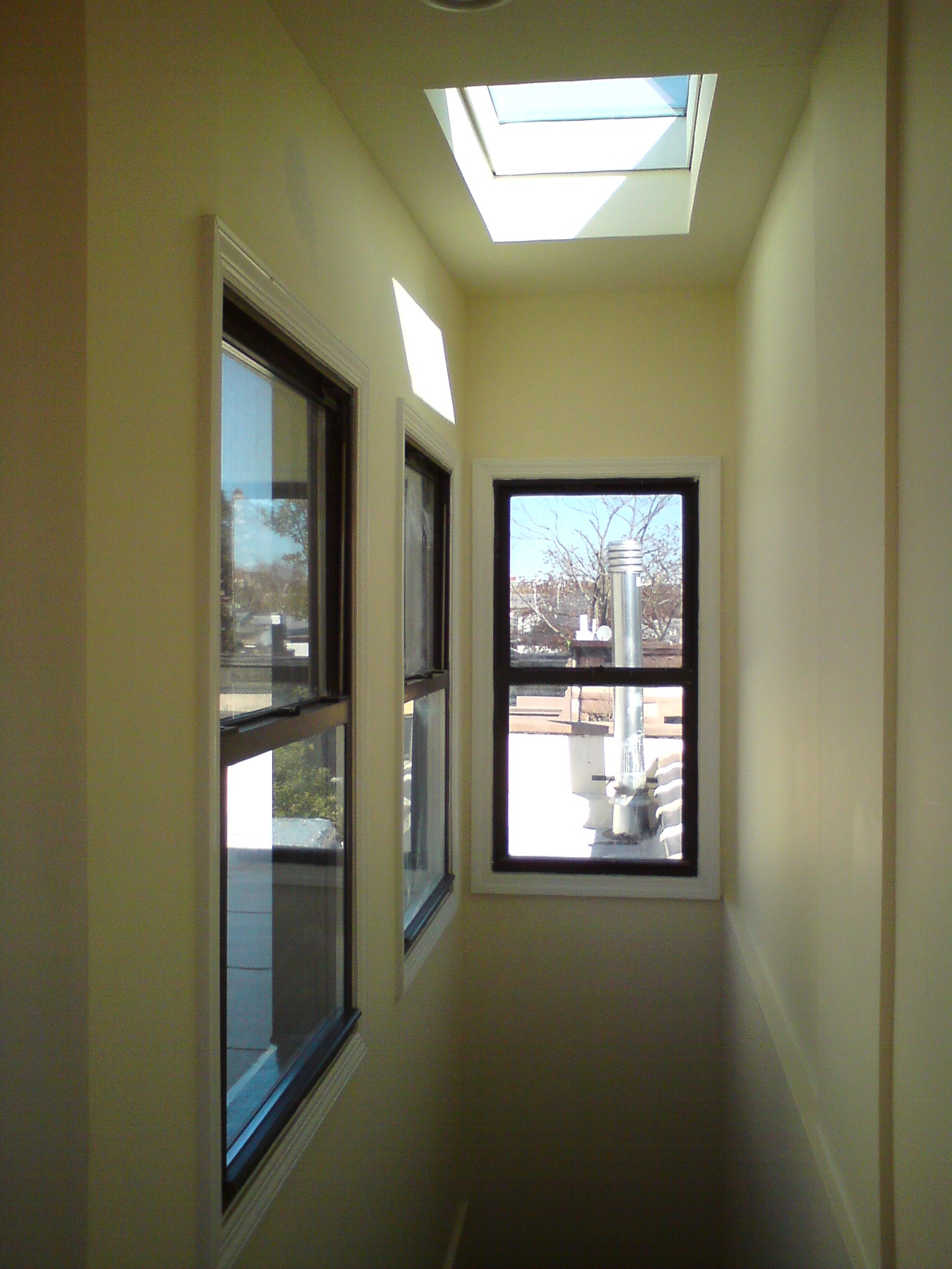 Narrow hallway with skylight and black-framed windows overlooking rooftop