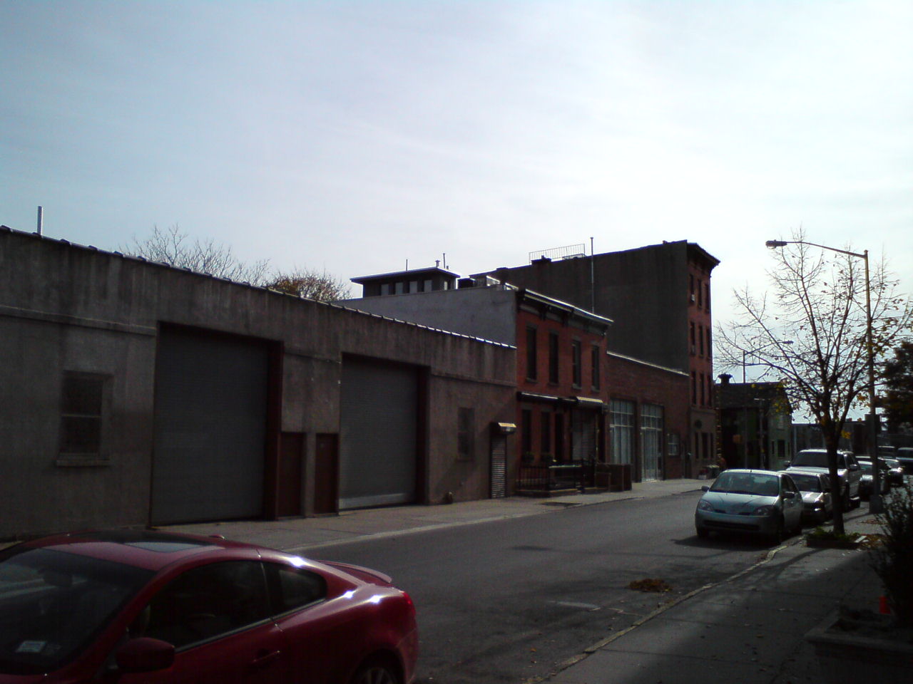Industrial brick and concrete buildings on urban street with parked cars.