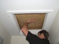 Person installing or adjusting wooden roof hatch panel from inside ceiling opening
