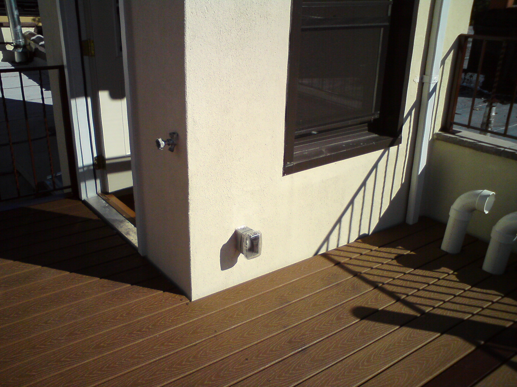 Exterior wall outlet on cream-colored building column with wooden deck flooring and windows