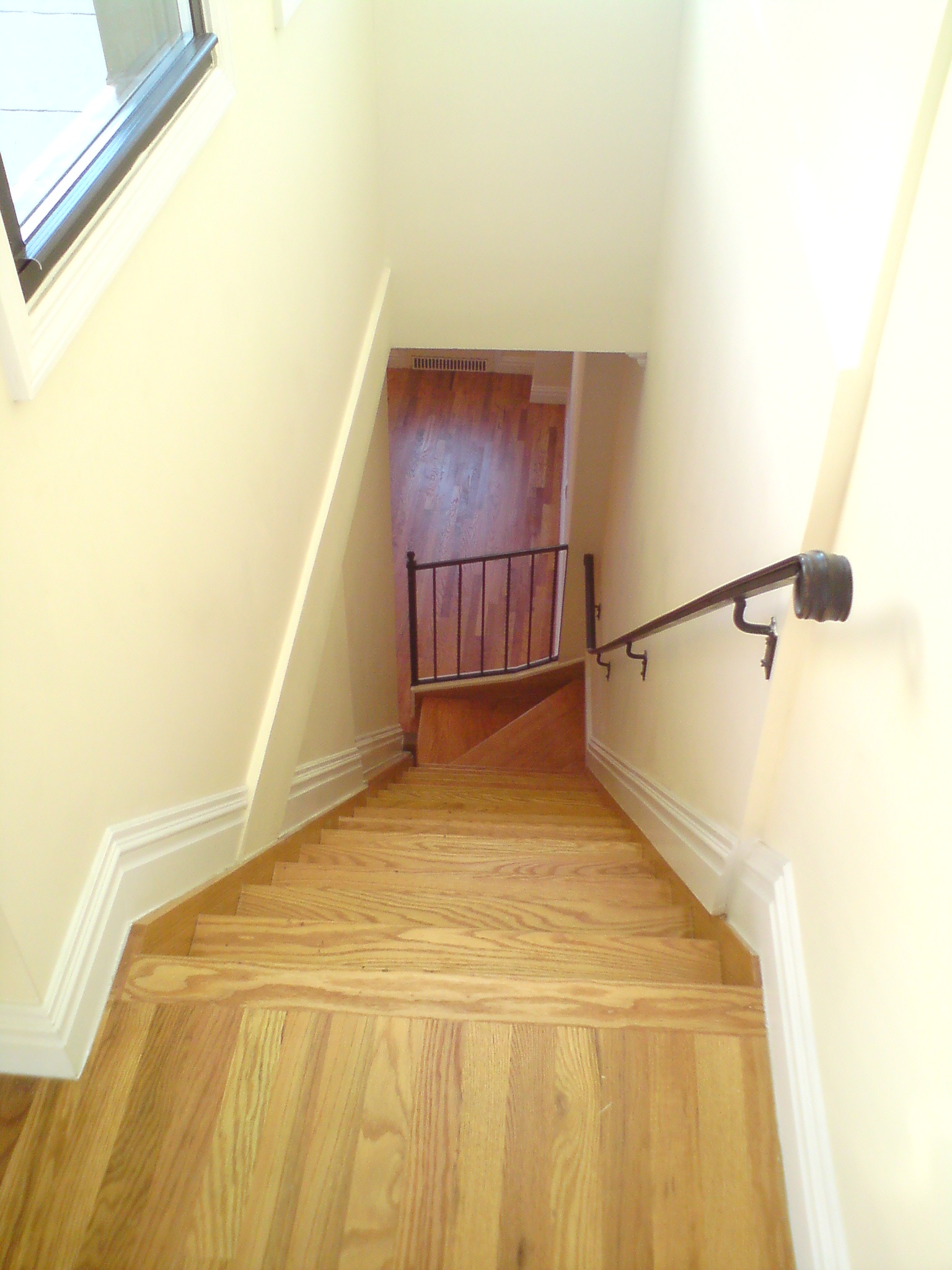 Interior stairwell with wooden treads, cream walls, metal railing, and natural window light.