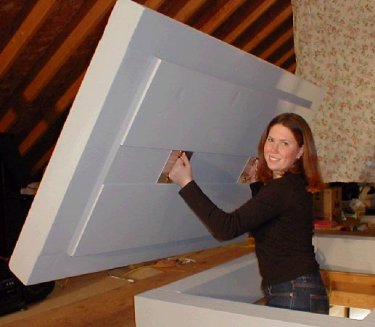 Woman in black jacket holding large blue roof panel indoors