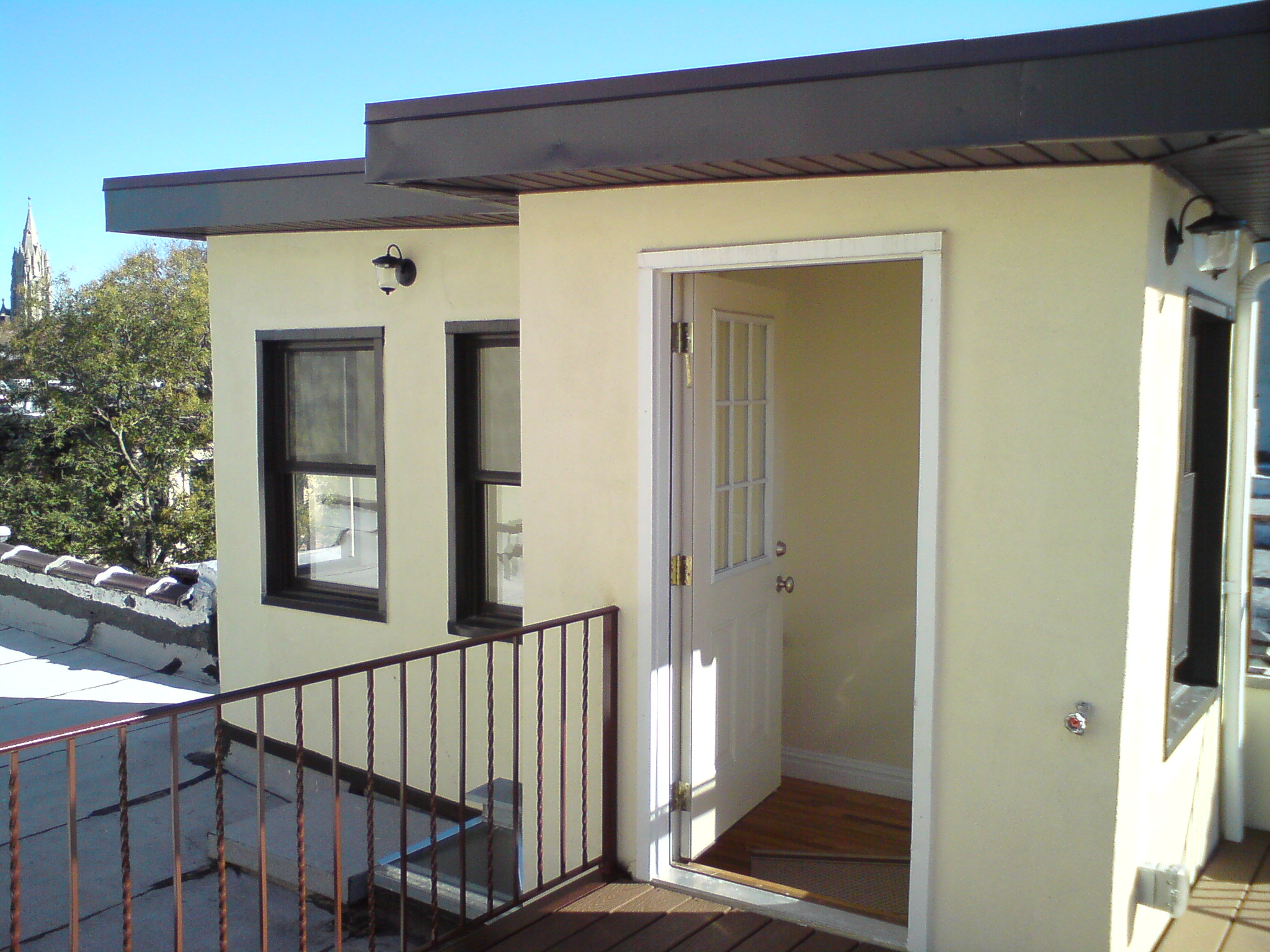 Modern yellow-painted roof deck addition with black metal overhang, railing, and glass doors.