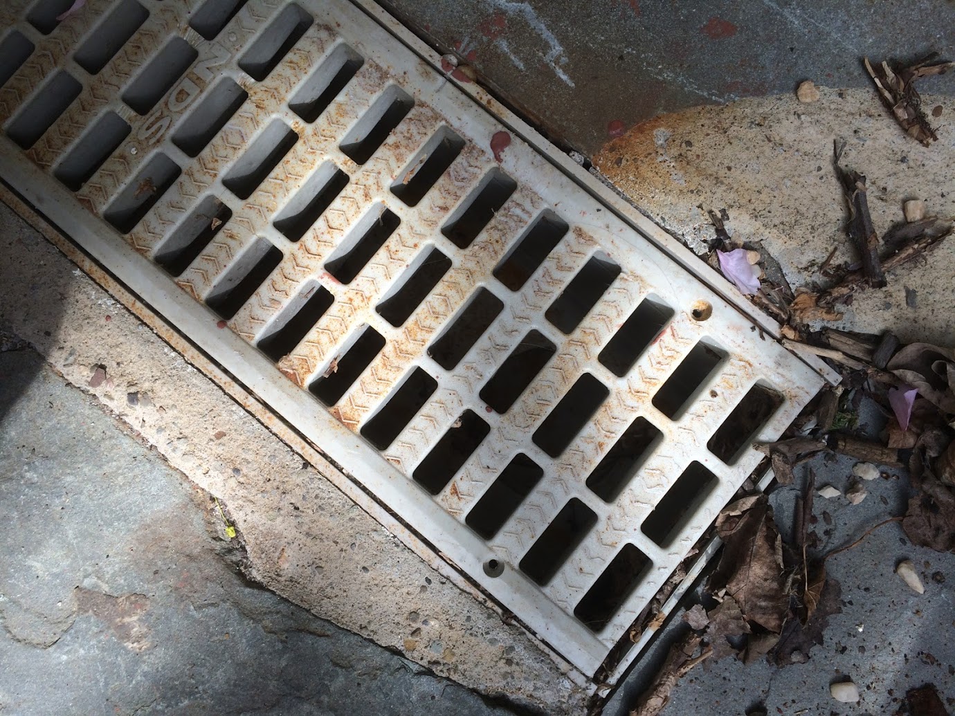 Overhead view of white plastic drainage grate with rectangular slots, surrounded by soil and garden debris.