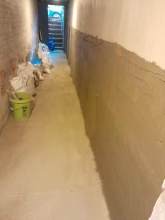 Narrow hallway with bare walls and concrete floor during renovation, doorway visible at end
