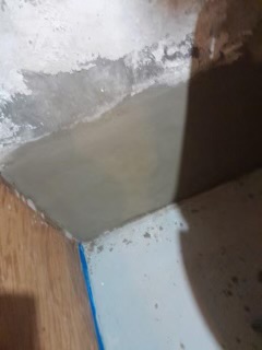 Concrete basement floor with patching compound and blue tape during renovation.
