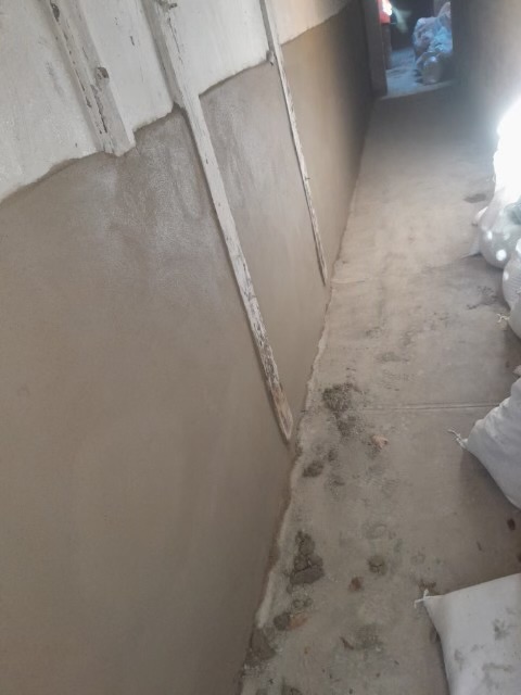 Narrow basement corridor with freshly poured wet concrete floor and white wall panels.