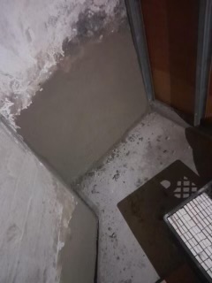 Overhead view of basement concrete floor with white wall, dark doorway, and work-in-progress flooring installation.