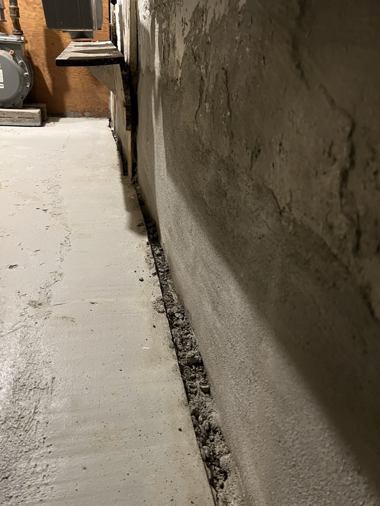 Narrow concrete corridor with finished wall and debris-filled floor gap.